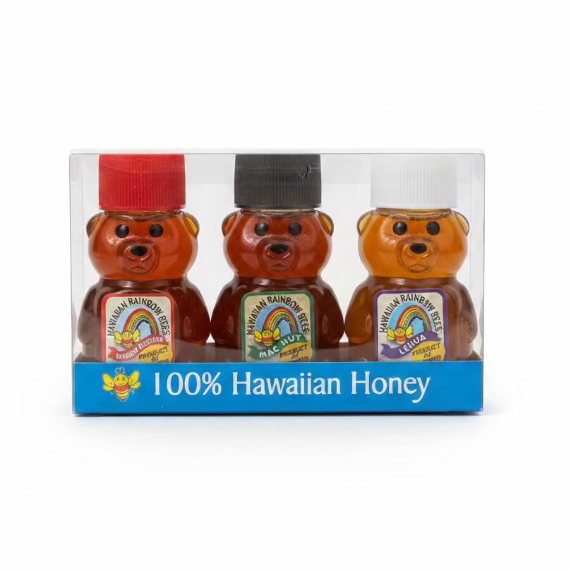 Three bear-shaped honey jars with colorful caps in a clear packaging box on a gray surface.